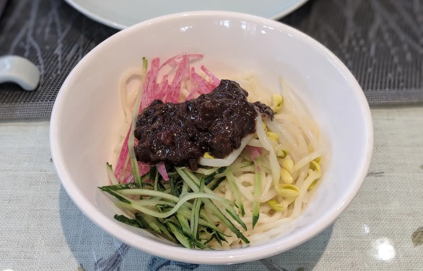 A bowl of Beijing zhajiangmian noodles with a dark soybean-paste sauce and vegetable toppings